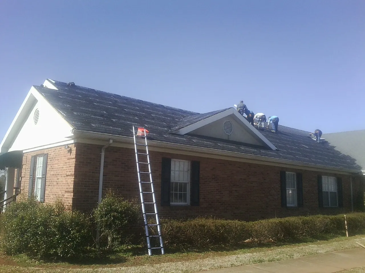 Crew tearing shingles off a brick ranch roof with a ladder set — Metal Roof Repair work by our crew in Swansea