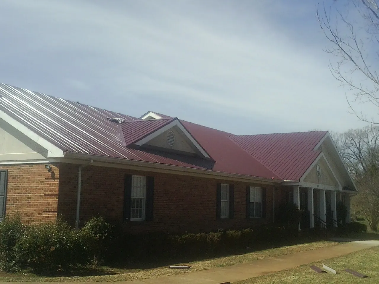 Red metal roof with gabled entries on a long brick building, from a Hail Damage Roof Repair job in Swansea
