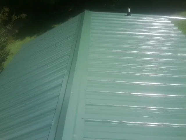 New green metal panels meeting at the ridge of a roof — Flat Roof Repair work by our crew in Swansea